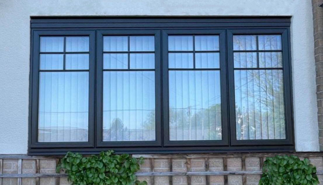 Large black uPVC casement window with elegant Georgian bars installed on a white rendered house wall above a wooden garden trellis.