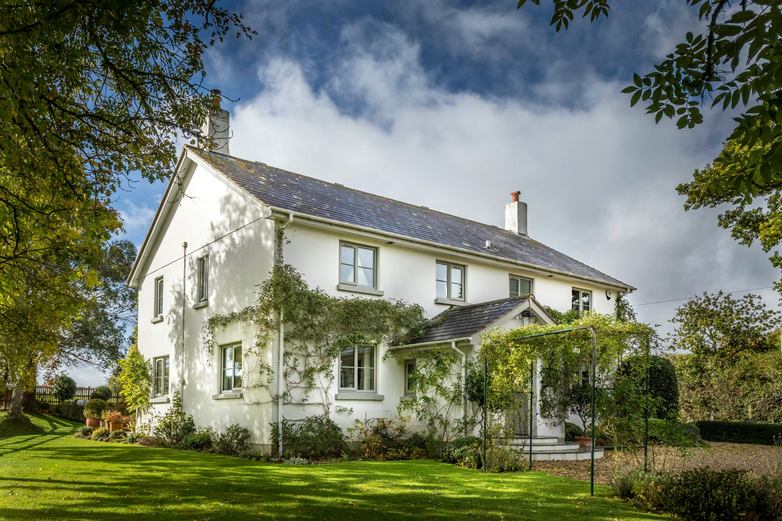 Large white country house exterior fitted with heritage sage green uPVC casement windows, surrounded by climbing green ivy and garden lawn
