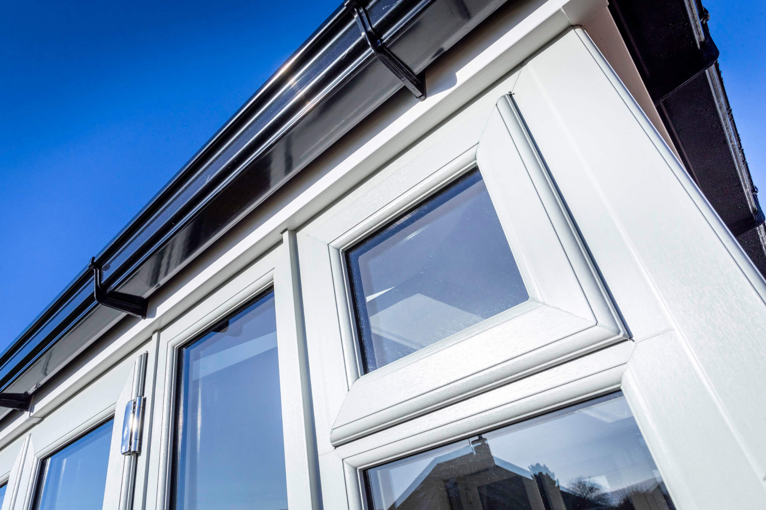 Up-close angle of a white sculptured uPVC window frame positioned underneath black roofline fascia boards and guttering